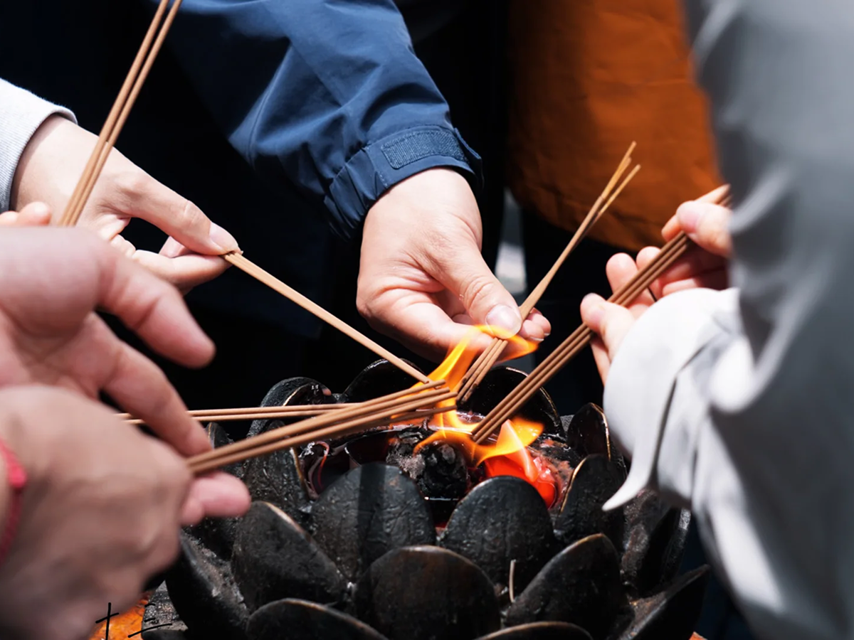 Visitors holding incense before a lotus-shaped temple burner